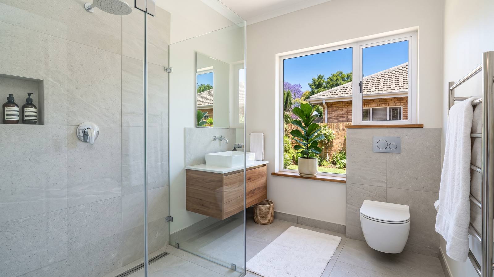 Renovated bathroom with a frameless walk-in shower, large grey porcelain wall tiles, a floating vanity and a wall-hung toilet, in natural light.