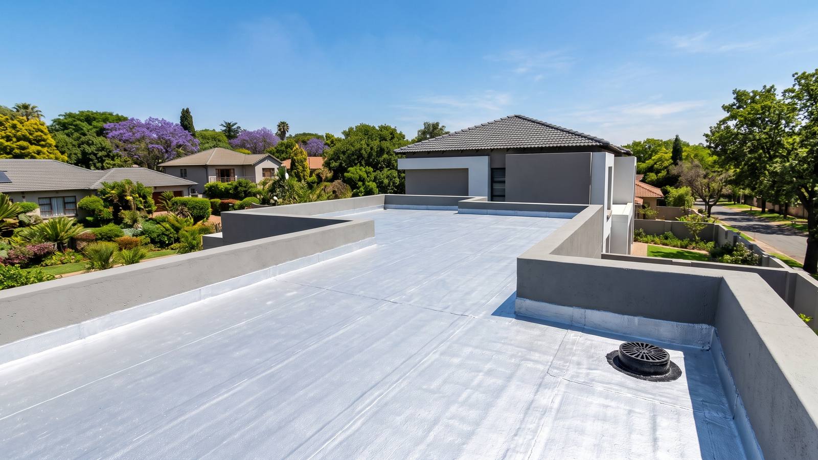 New silver-coated torch-on waterproofing membrane on a flat concrete roof with a parapet wall and an outlet, on a modern Johannesburg house.
